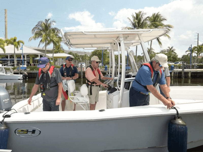 Female trainer with life jacket doing a demonstration with trainees on boat docked in marina.